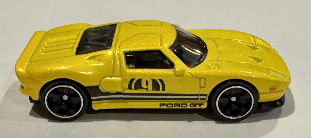 Matchbox yellow 2005 Ford GT side view showing number 9 graphics, black Ford GT stripes, and black wheels with silver rims.